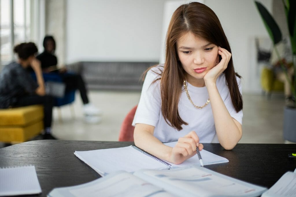 thoughtful asian woman with textbook in classroom